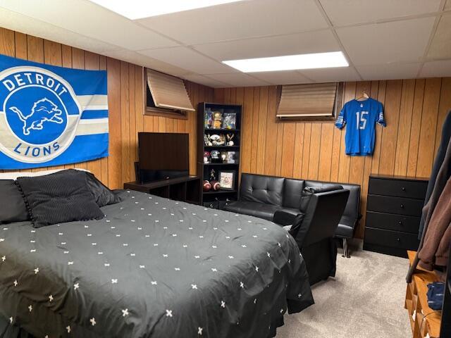 carpeted bedroom with a paneled ceiling and wood walls