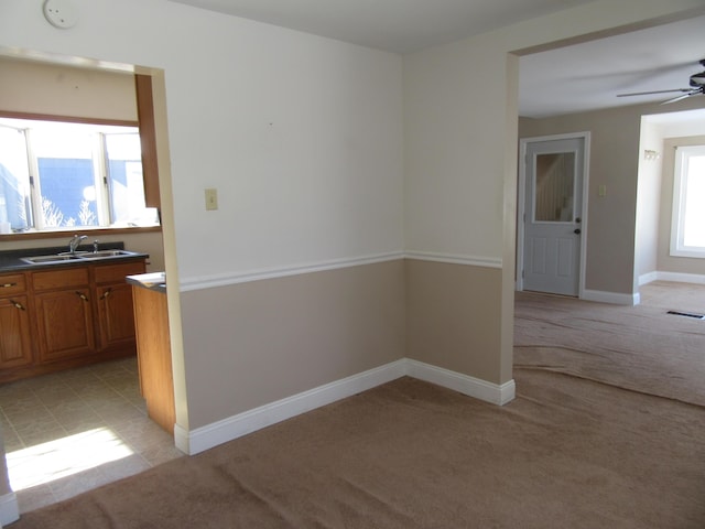 carpeted empty room featuring ceiling fan, sink, and a healthy amount of sunlight