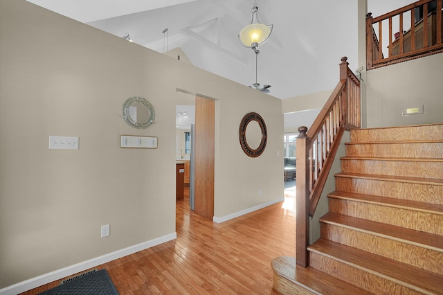 stairs with hardwood / wood-style floors and high vaulted ceiling