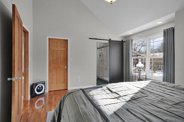 bedroom featuring high vaulted ceiling, a barn door, and light wood-type flooring