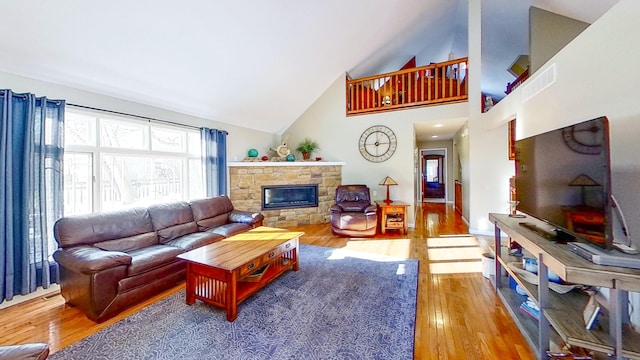 living room with a stone fireplace, high vaulted ceiling, and hardwood / wood-style flooring