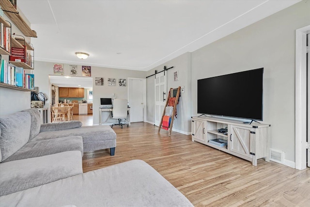 living room featuring light wood-type flooring, a barn door, and baseboards
