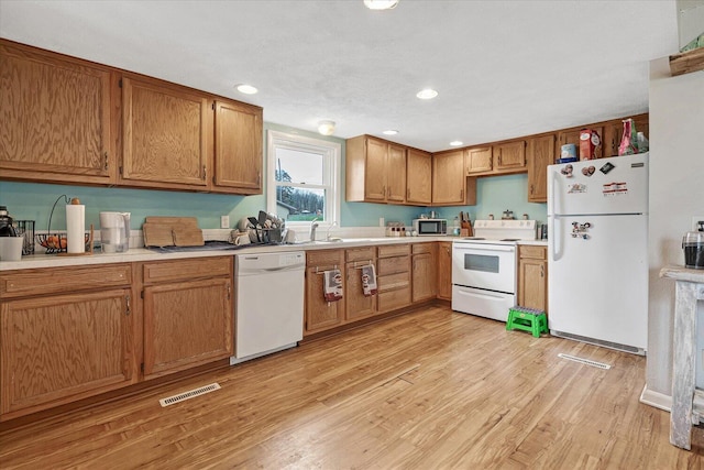 kitchen featuring white appliances, light countertops, light wood finished floors, brown cabinets, and recessed lighting