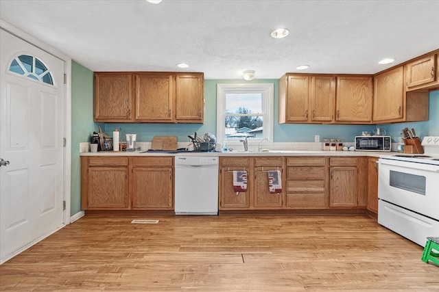 kitchen featuring white appliances, a sink, brown cabinets, light countertops, and recessed lighting