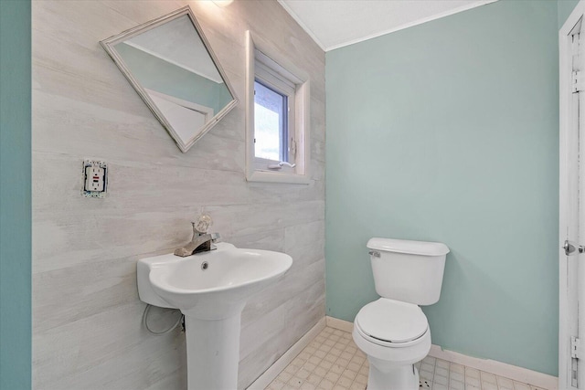 half bathroom with toilet, baseboards, tile patterned floors, and crown molding