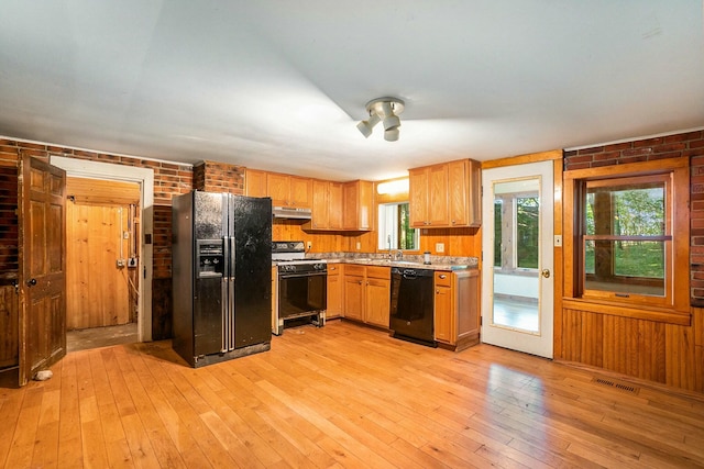 kitchen with light wood-type flooring, brick wall, sink, and black appliances