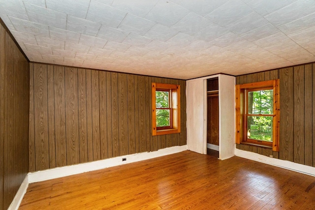 empty room featuring wood-type flooring, a wealth of natural light, and wooden walls