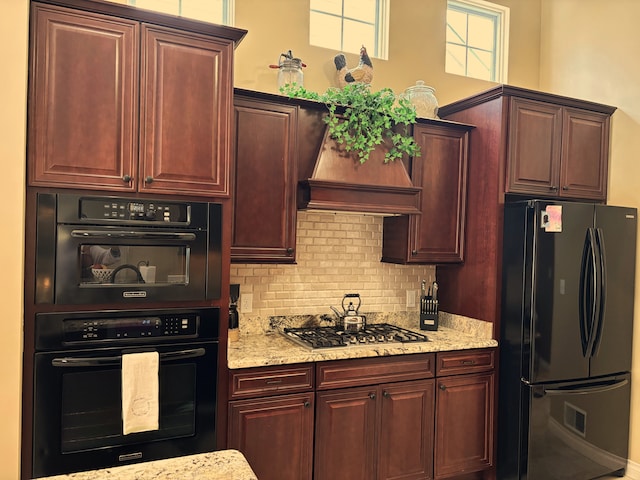 kitchen with decorative backsplash, wall chimney exhaust hood, light stone counters, and black appliances