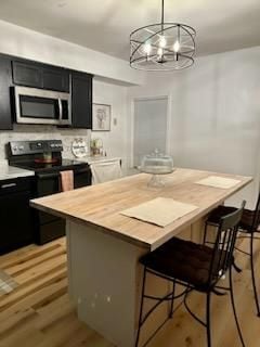 kitchen with a kitchen bar, hanging light fixtures, a chandelier, black electric range oven, and a center island