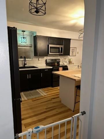 kitchen with backsplash, black electric range, pendant lighting, sink, and a kitchen breakfast bar