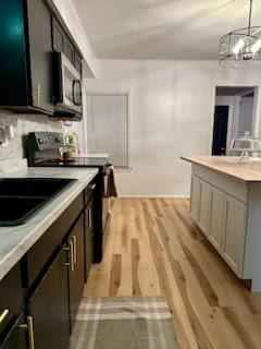 kitchen featuring hanging light fixtures, black range with electric stovetop, light wood-type flooring, and an inviting chandelier