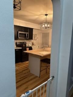 kitchen with decorative light fixtures, black range with electric stovetop, kitchen peninsula, a chandelier, and a breakfast bar area