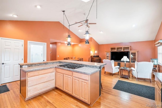 kitchen with stainless steel gas stovetop, light brown cabinetry, lofted ceiling, a kitchen island, and light hardwood / wood-style flooring