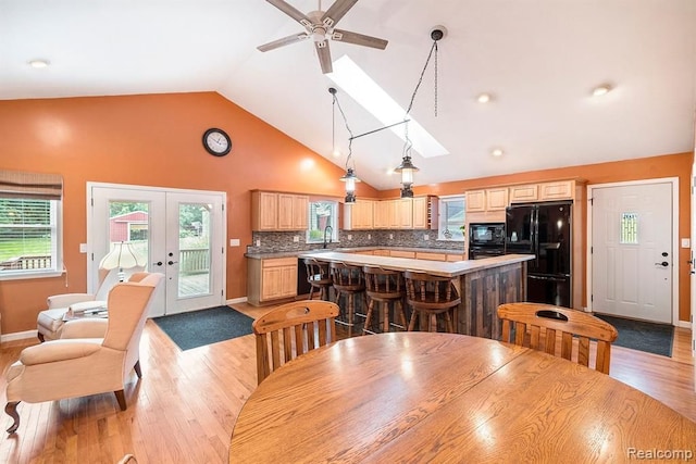 dining room featuring ceiling fan, light hardwood / wood-style floors, sink, a skylight, and french doors