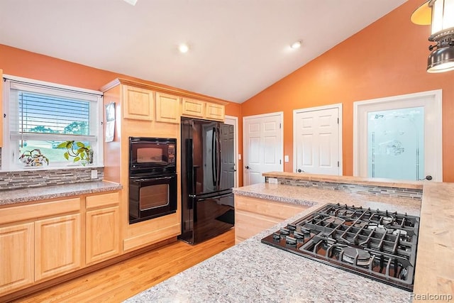 kitchen featuring light hardwood / wood-style floors, light brown cabinets, vaulted ceiling, light stone counters, and black appliances