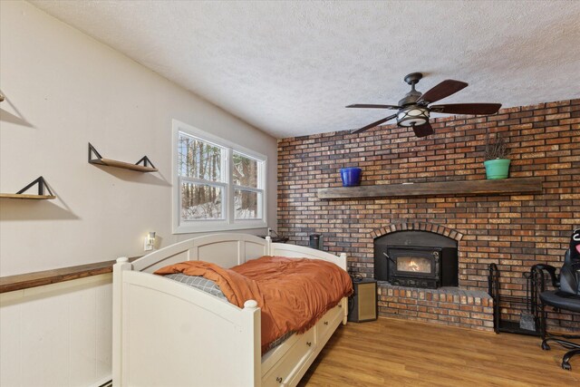 bedroom with a textured ceiling, ceiling fan, a wood stove, and light wood-type flooring