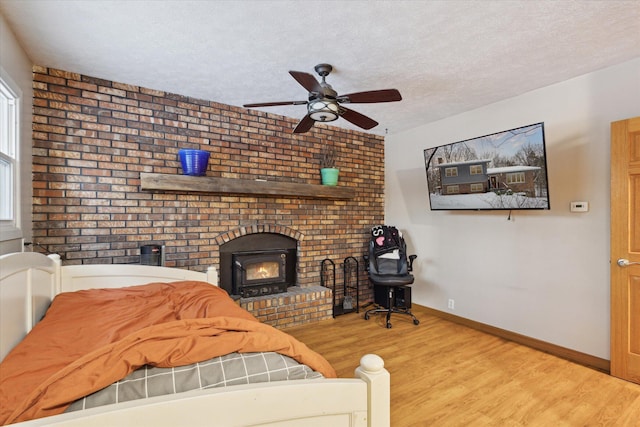 bedroom with a textured ceiling, ceiling fan, light hardwood / wood-style floors, and a wood stove