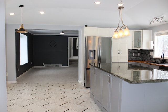 kitchen with stainless steel refrigerator with ice dispenser, sink, white cabinetry, hanging light fixtures, and dark stone counters