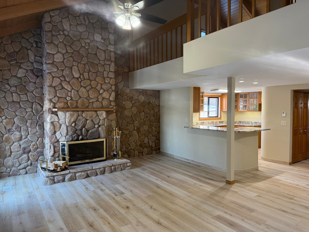 unfurnished living room featuring ceiling fan, a high ceiling, light hardwood / wood-style flooring, and a stone fireplace