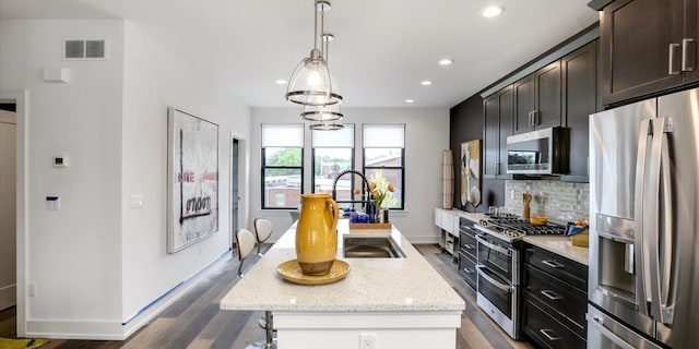 kitchen featuring appliances with stainless steel finishes, sink, light stone counters, and a center island with sink