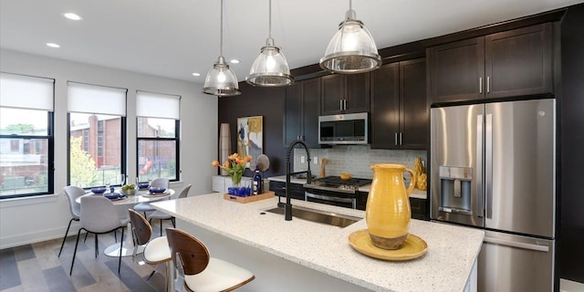 kitchen featuring tasteful backsplash, decorative light fixtures, a center island with sink, dark brown cabinetry, and appliances with stainless steel finishes