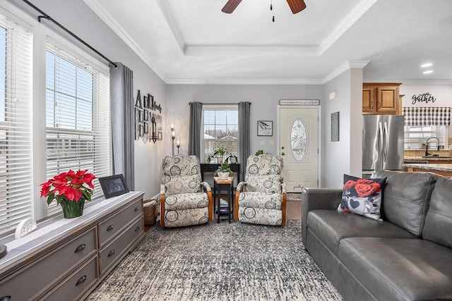 living room with ceiling fan, sink, a tray ceiling, and ornamental molding