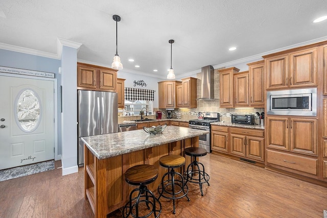 kitchen featuring decorative light fixtures, wall chimney range hood, a kitchen island, stainless steel appliances, and light stone counters