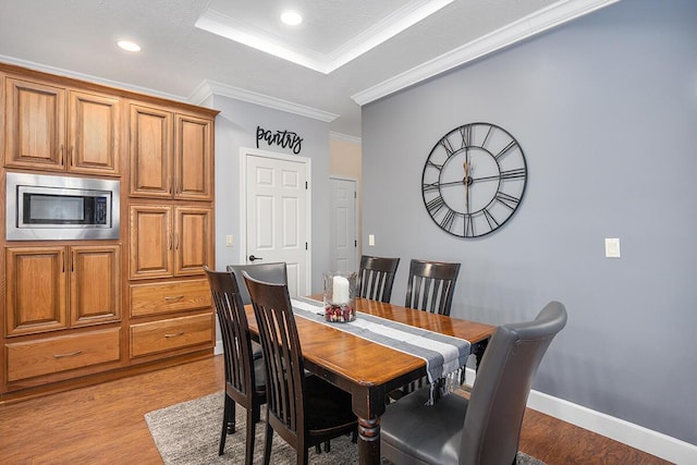 dining room with light wood-type flooring, ornamental molding, and a raised ceiling