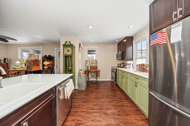 kitchen with green cabinets, appliances with stainless steel finishes, ceiling fan, dark wood-type flooring, and sink