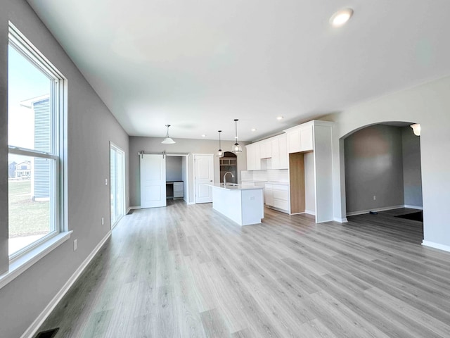 unfurnished living room featuring a barn door, light wood-type flooring, and sink