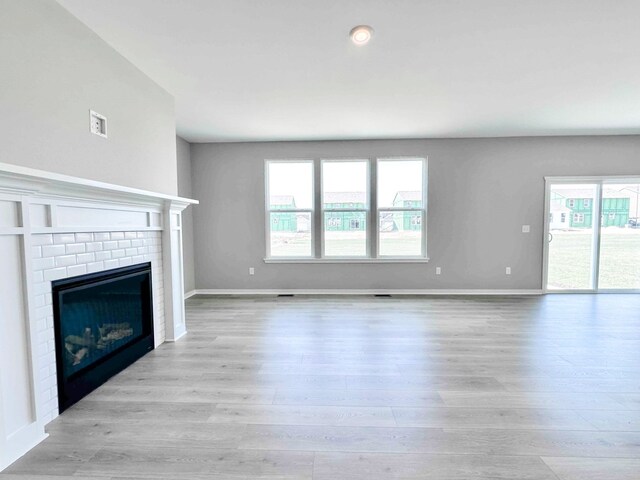 unfurnished living room with a brick fireplace and light hardwood / wood-style flooring