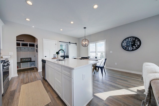 kitchen with a barn door, a center island with sink, appliances with stainless steel finishes, decorative light fixtures, and white cabinets