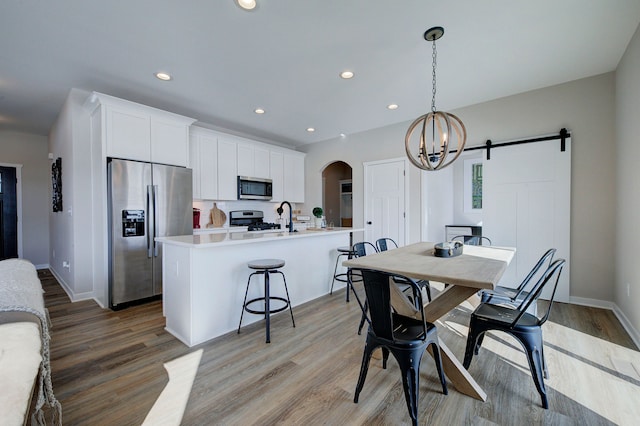 dining space with light hardwood / wood-style floors, a barn door, and an inviting chandelier