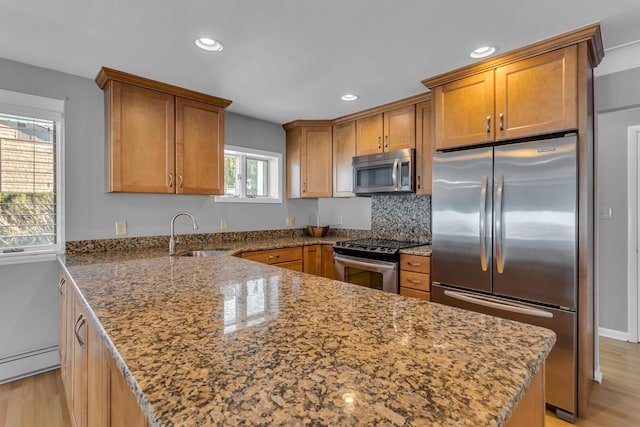 kitchen with stone counters, sink, light wood-type flooring, stainless steel appliances, and baseboard heating