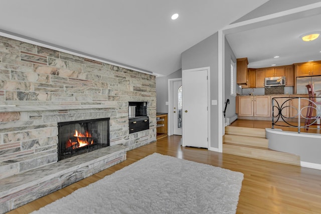 living room featuring sink, lofted ceiling, a stone fireplace, and light wood-type flooring