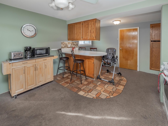 kitchen with a toaster, light colored carpet, a peninsula, a ceiling fan, and brown cabinets