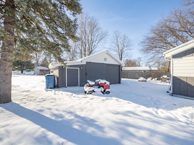 snowy yard featuring a garage, an outbuilding, fence, and a storage shed