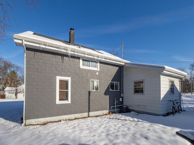 snow covered back of property featuring a chimney