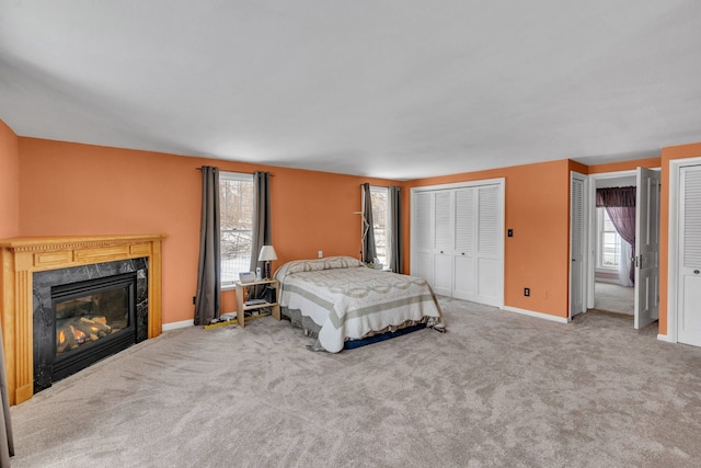 bedroom featuring a fireplace, two closets, multiple windows, and carpet flooring