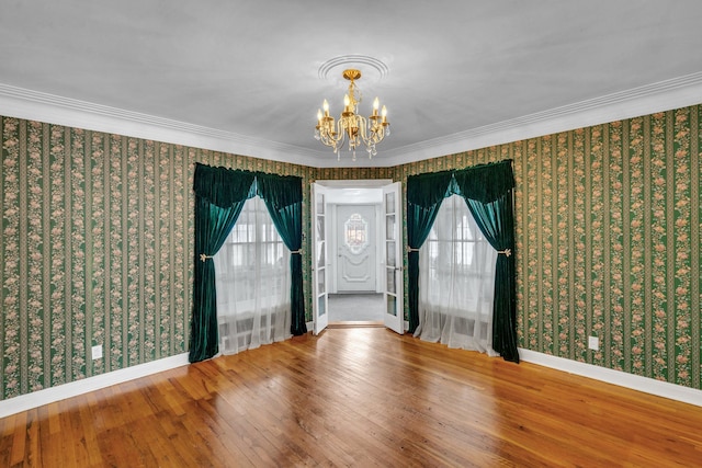 spare room with a wealth of natural light, an inviting chandelier, ornamental molding, and hardwood / wood-style flooring