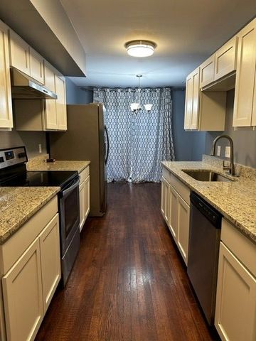 kitchen with stainless steel appliances, dark wood-type flooring, hanging light fixtures, light stone counters, and sink