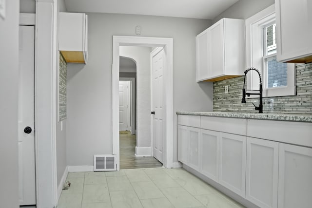 kitchen featuring backsplash, sink, light stone counters, and white cabinetry