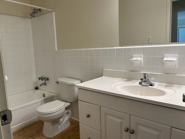 full bathroom featuring hardwood / wood-style floors, tiled shower / bath combo, vanity, tile walls, and toilet