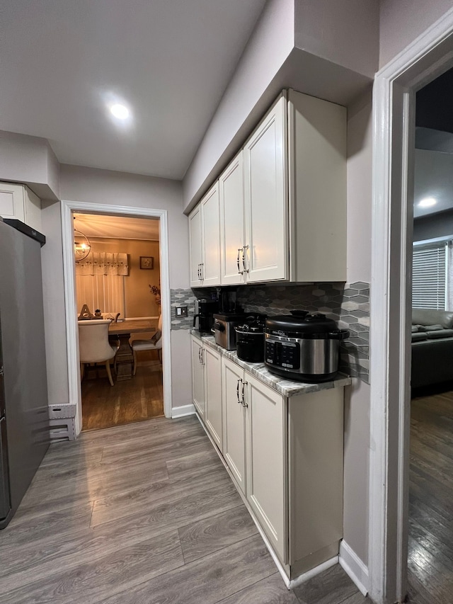 kitchen with decorative backsplash, light hardwood / wood-style floors, white cabinets, and light stone counters