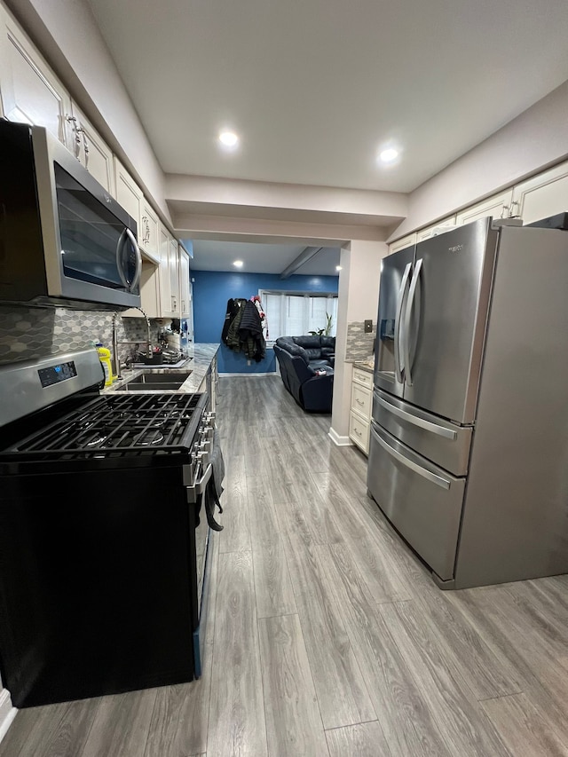 kitchen featuring appliances with stainless steel finishes, decorative backsplash, white cabinets, light hardwood / wood-style flooring, and sink