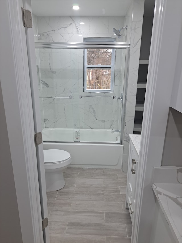 full bathroom with combined bath / shower with glass door, vanity, and toilet