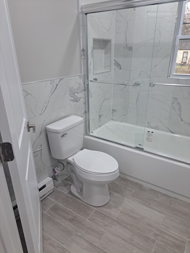 bathroom featuring a baseboard heating unit, bath / shower combo with glass door, tile walls, and toilet