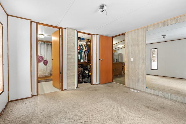 unfurnished bedroom with light carpet, connected bathroom, stainless steel fridge, and wooden walls