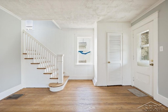 entrance foyer featuring a textured ceiling, a wealth of natural light, ornamental molding, and light hardwood / wood-style floors