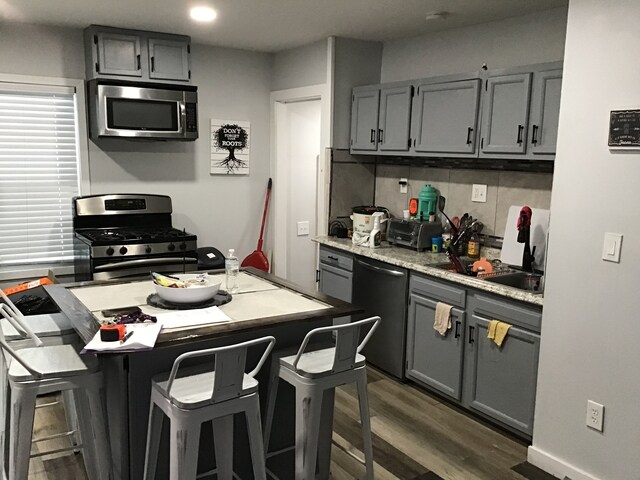 kitchen featuring dark wood-type flooring, gray cabinets, backsplash, stainless steel appliances, and a kitchen bar